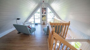 Een loft-achtige kamer met een schuine plafond, houten vloer, een blauwe bank, een houten bankje en een klein beeldje.