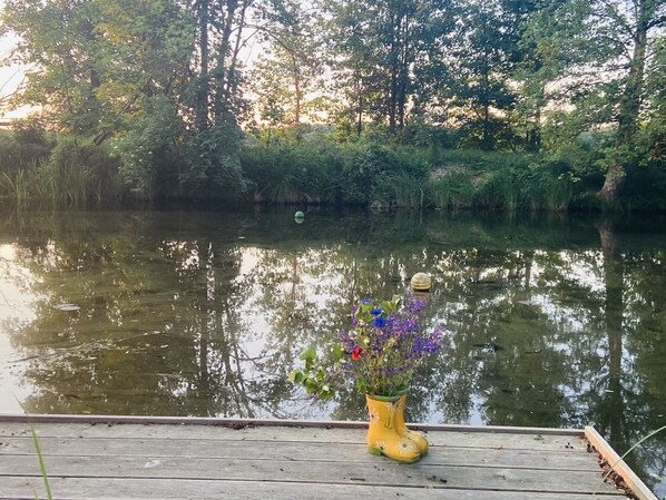 Une jetée en bois sur laquelle est posé un jardinier en forme de botte jaune, rempli de fleurs.