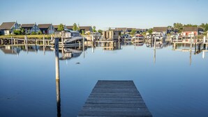 Een jachthaven met aangemeerde boten, een houten steiger en woongebouwen op de achtergrond.