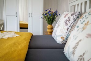 Een bed met een gele deken, een vaas met bloemen en een kussen met dessin.