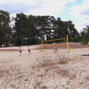 Un terrain de volley-ball avec un filet, entouré de sable et d’arbres.