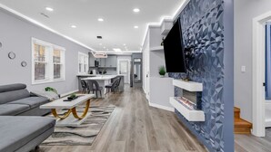 A modern living room with a grey sofa, a dining area with a white table, and a kitchen in the background. - Spacious House in Charlotte Close to NoDa District (Charlotte)