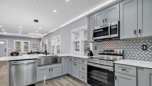 A modern kitchen with grey cabinetry, stainless steel appliances, and a herringbone-patterned backsplash. - Spacious House in Charlotte Close to NoDa District (Charlotte)