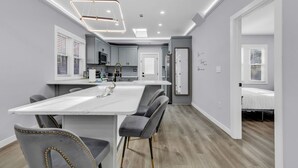 A modern kitchen with a central island, grey upholstered chairs, and a pendant light fixture. - Spacious House in Charlotte Close to NoDa District (Charlotte)
