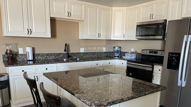 A modern kitchen with white cabinetry, granite countertops, a stainless steel refrigerator, a microwave, and an oven. - 2 Bedroom Suite in Ridgecrest  (Ridgecrest)