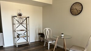 A room with a wooden floor, a white chair, a small table, a bookshelf, and a wall clock. - 2 Bedroom Suite in Ridgecrest  (Ridgecrest)