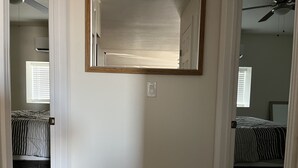 A bedroom with a large mirror, two beds with striped bedding, a ceiling fan, and a window with blinds. - 2 Bedroom Suite in Ridgecrest  (Ridgecrest)