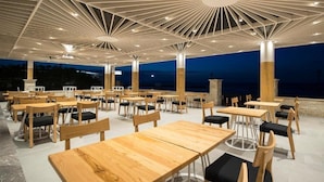 An outdoor dining area with wooden tables and chairs, a modern ceiling design, and a view of the sea at dusk. - Insula Alba Resort and Spa - Adults Only (Hersonissos)