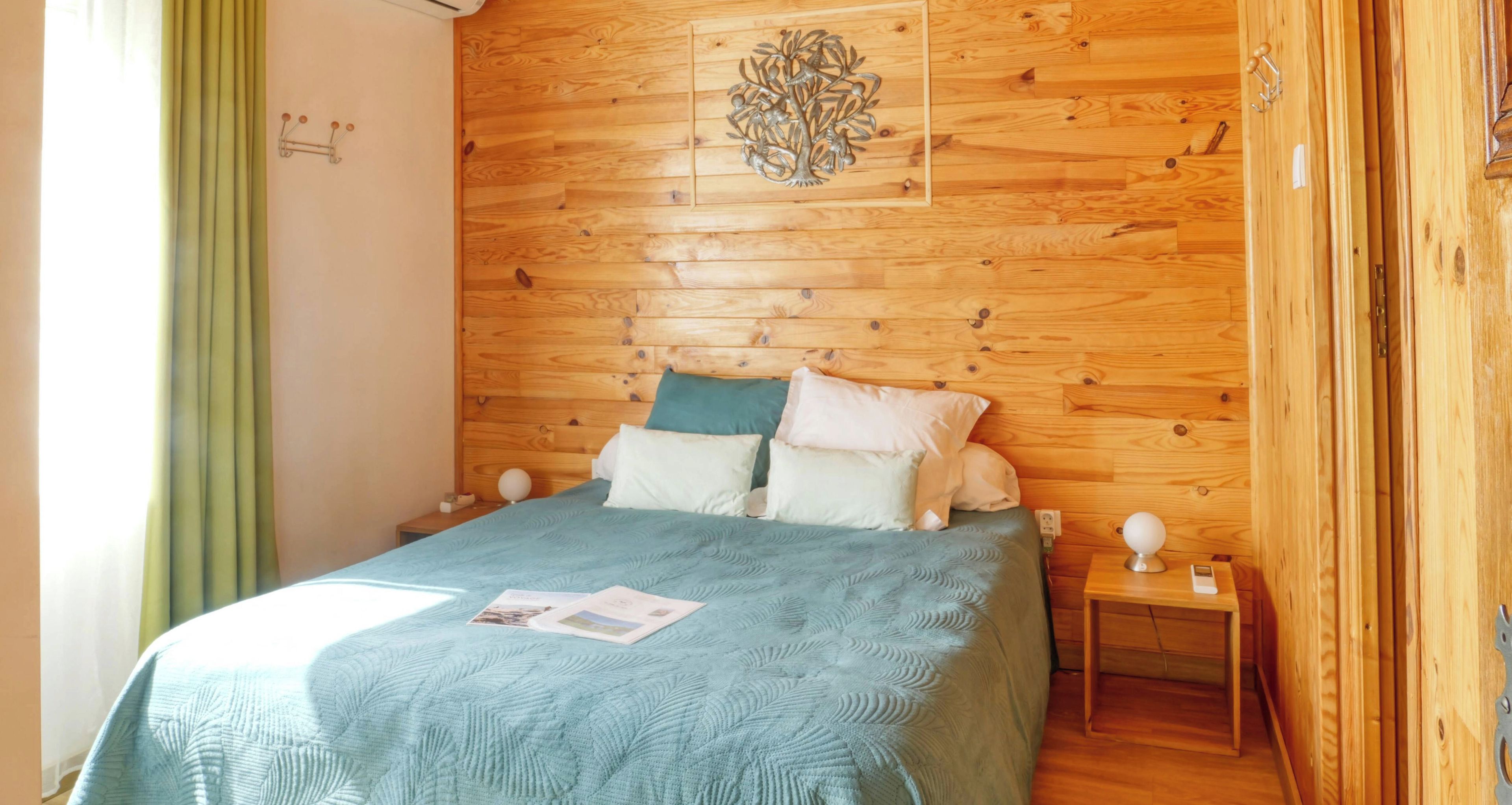 Camera da letto con rivestimento in legno, un letto, cuscini, un comodino e un elemento decorativo a parete.