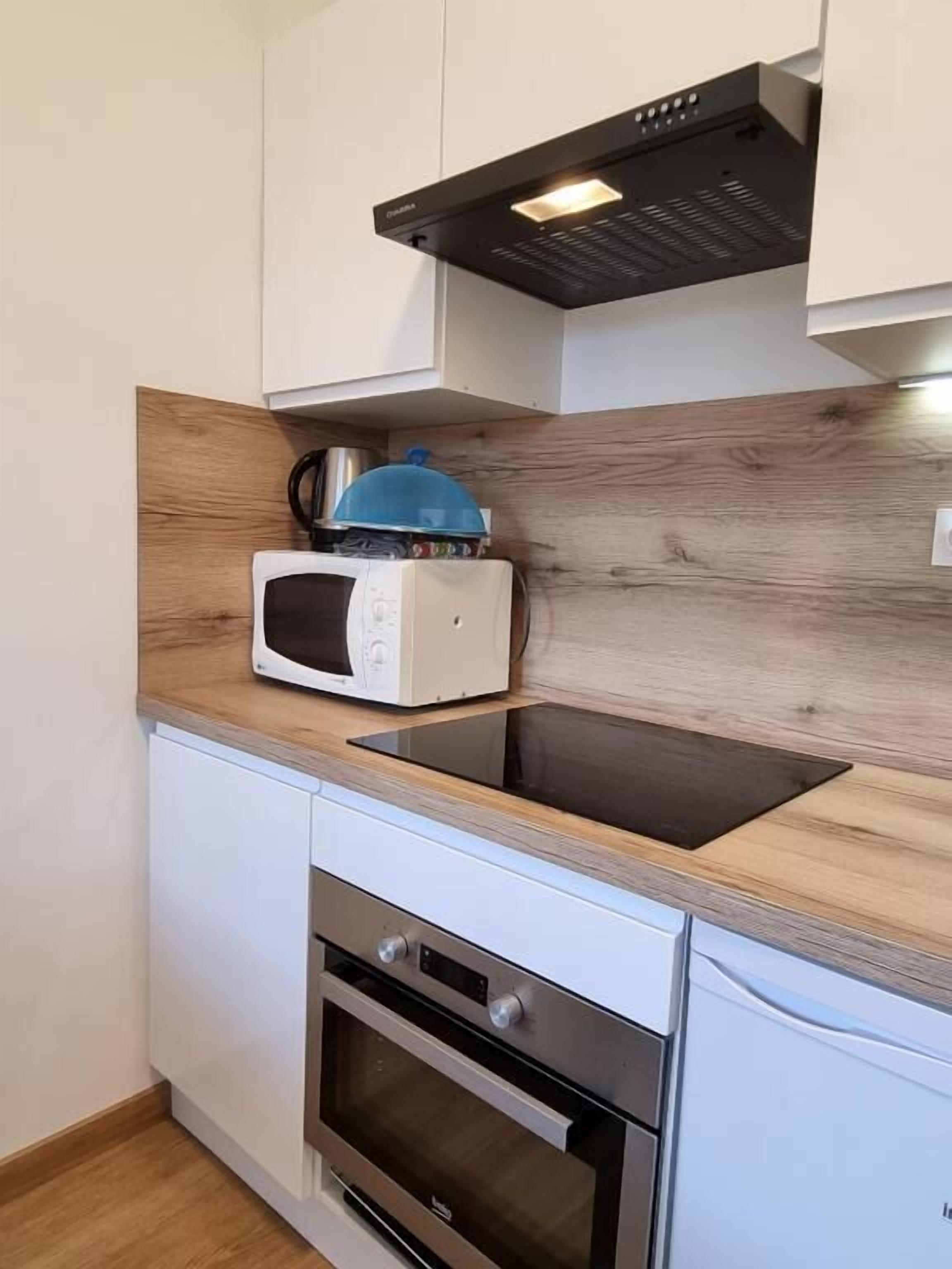Una cocina compacta con microondas, hervidor y horno empotrado.