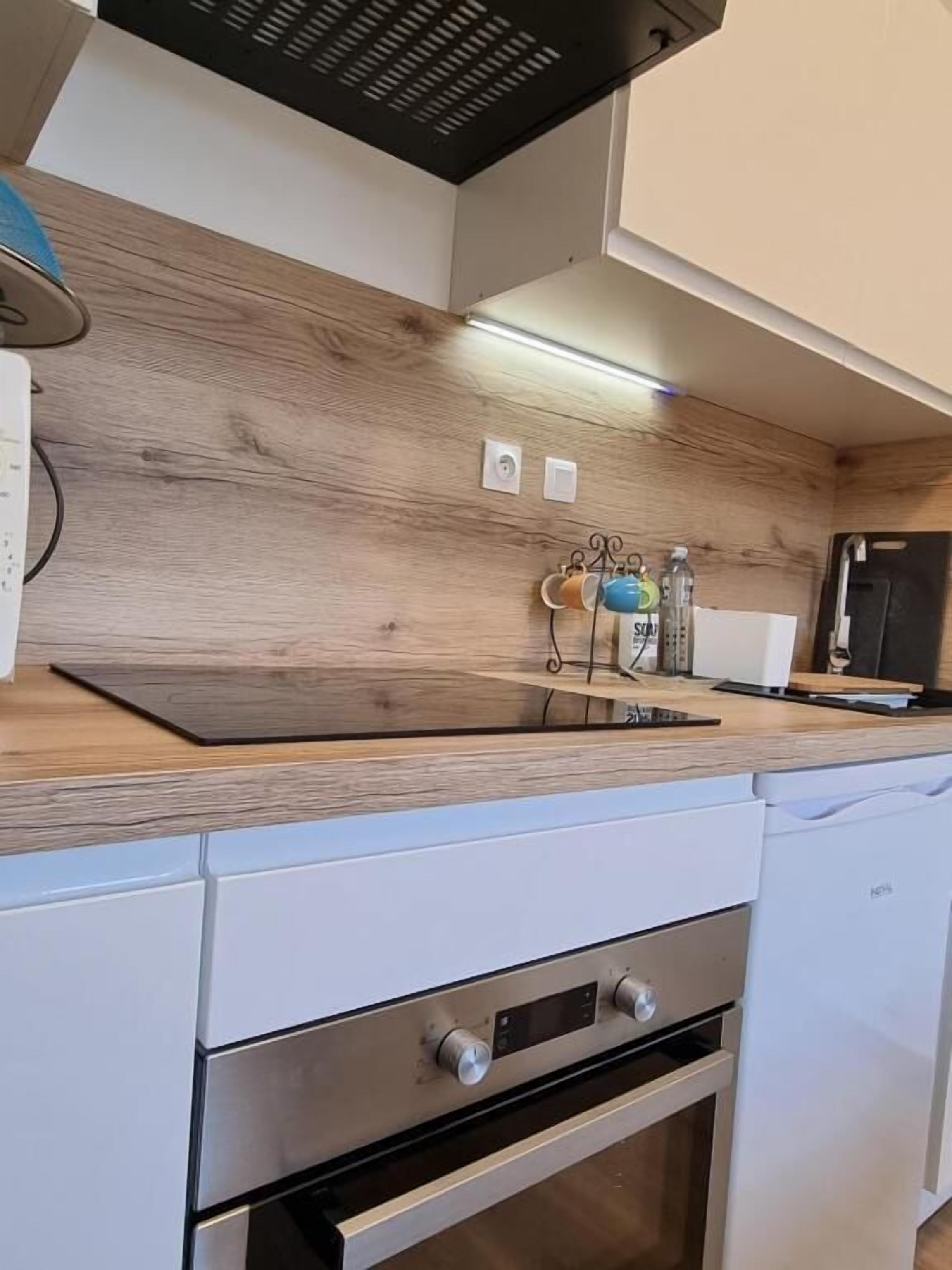 A modern kitchen with wooden cabinetry, a built-in oven, and a countertop with a kettle and water bottles.