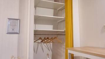 A room with a wooden ceiling, a white wall, a yellow curtain, a white desk, a white chair, and a metal hanger rack.
