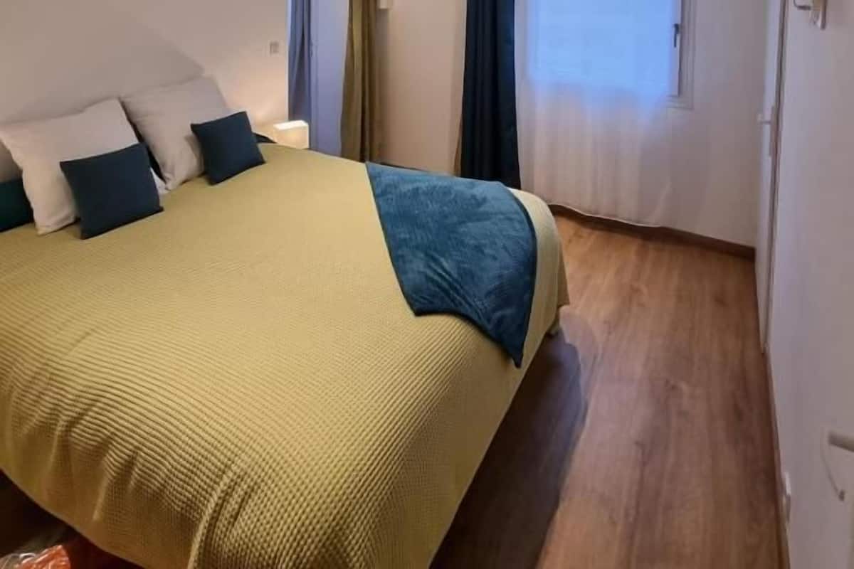 Une chambre à coucher avec un lit, des rideaux, une télévision et une fenêtre.
