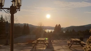 A sunset view from a rooftop terrace with picnic tables and a street lamp. - Les Tables Aux Vaches (La Salvetat-sur-Agout)