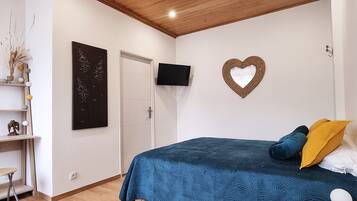 A bedroom with a bed, a TV, a heart-shaped decoration, and a shelf with decorative items.
