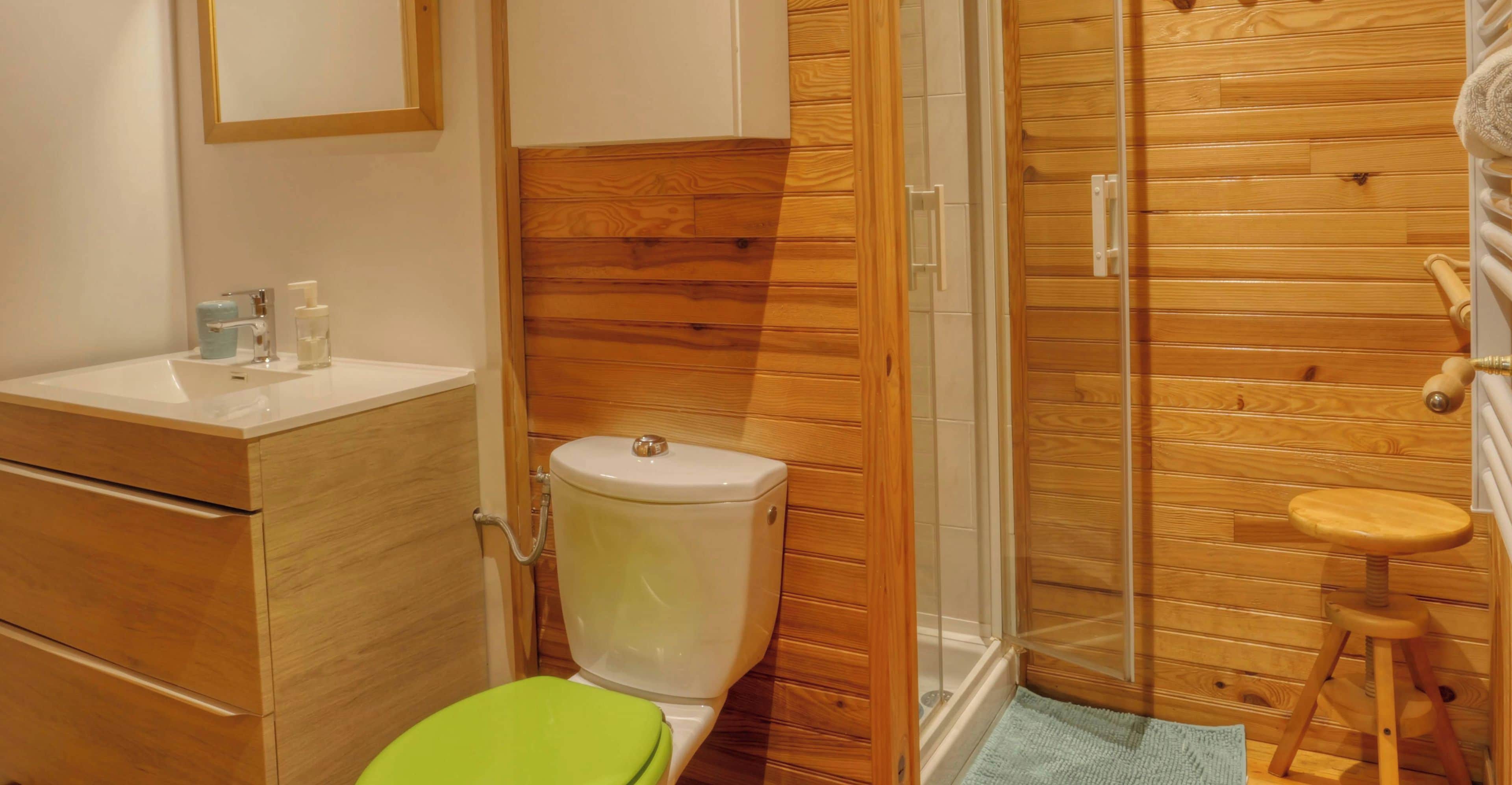 A bathroom with a wooden vanity, a toilet, a shower enclosure, and a small stool.