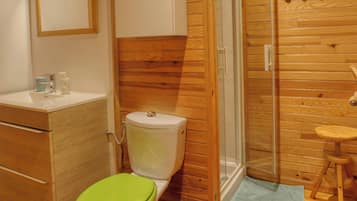 A bathroom with a wooden vanity, a toilet, a shower enclosure, and a small stool.