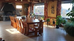 A dining area with a large wooden table and chairs, a built-in stove, and potted plants. - Les Tables Aux Vaches (La Salvetat-sur-Agout)