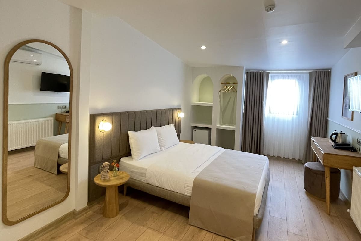 A hotel room with a large bed, a desk, a mirror, and a view of the outside.