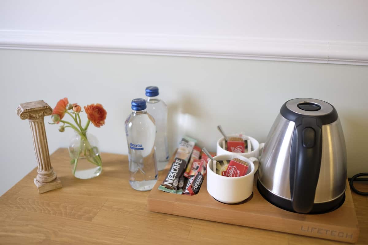 A wooden table with a coffee maker, a vase with flowers, a water bottle, and a tray with snacks.