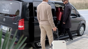 A black van with a luggage cart and a person in a beige outfit standing beside it. - Meshk Airport hotel (Arnavutköy)