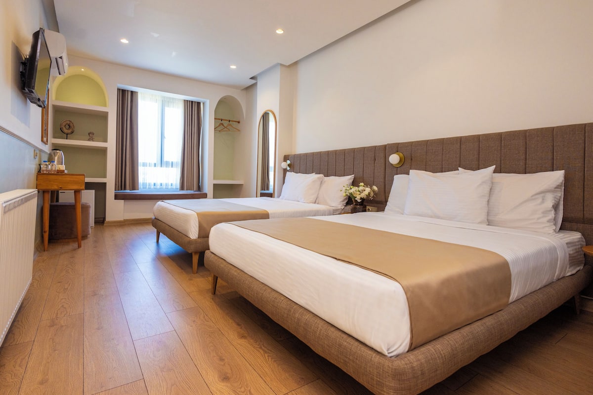 A hotel room with two beds, a desk, a mirror, and a window with curtains.