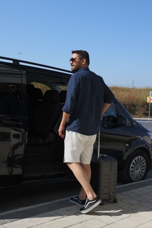 Une personne se tient à côté d’un fourgon noir, une valise à la main.