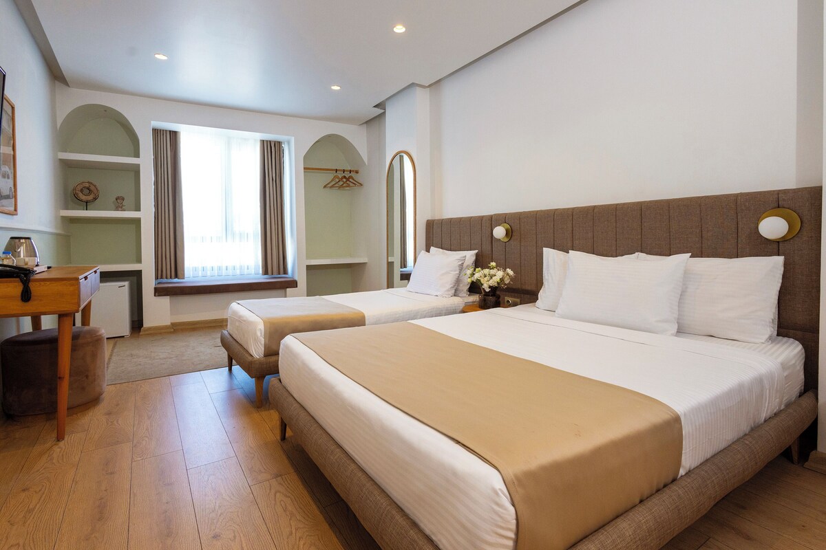 A hotel room with two beds, a desk, a chair, a small table, and a window with curtains.