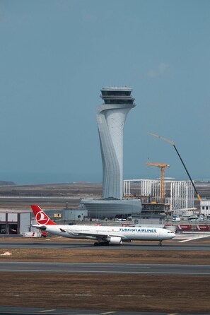 Un avion de Turkish Airlines sur la piste, avec une tour de contrôle et des grues de construction en arrière-plan.