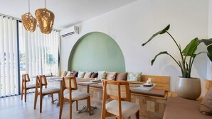 A modern dining area with wooden chairs and a bench, a large potted plant, and a round green accent wall. - Meshk Airport hotel (Arnavutköy)