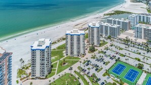 A high-rise hotel with multiple floors, a beach view, and a tennis court.