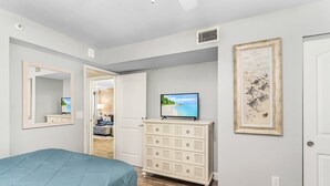 A bedroom with a bed, dresser, TV, and artwork.
