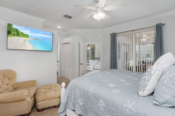A bedroom with a bed, a chair, a television, and a ceiling fan.