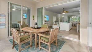 Um pátio espaçoso com mesa e cadeiras de madeira, ventilador de teto e vista para a sala de estar.