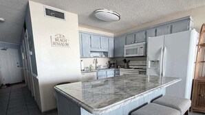 Una cocina con una isla de mármol, gabinetes grises y un letrero que dice 'Beach Bungalow'.