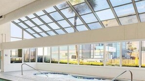 Una piscina interior con techo de vidrio, ventanas transparentes y suelo de baldosas.