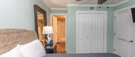 A bedroom with a bed, a ceiling fan, a door, and a nightstand with a lamp.