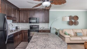 A modern kitchen with dark wood cabinets, a granite countertop, a built-in oven, and a ceiling fan.