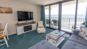 Un salon moderne doté d’un téléviseur à écran plat, d’un canapé, d’une table basse et d’un balcon offrant une vue sur la mer.