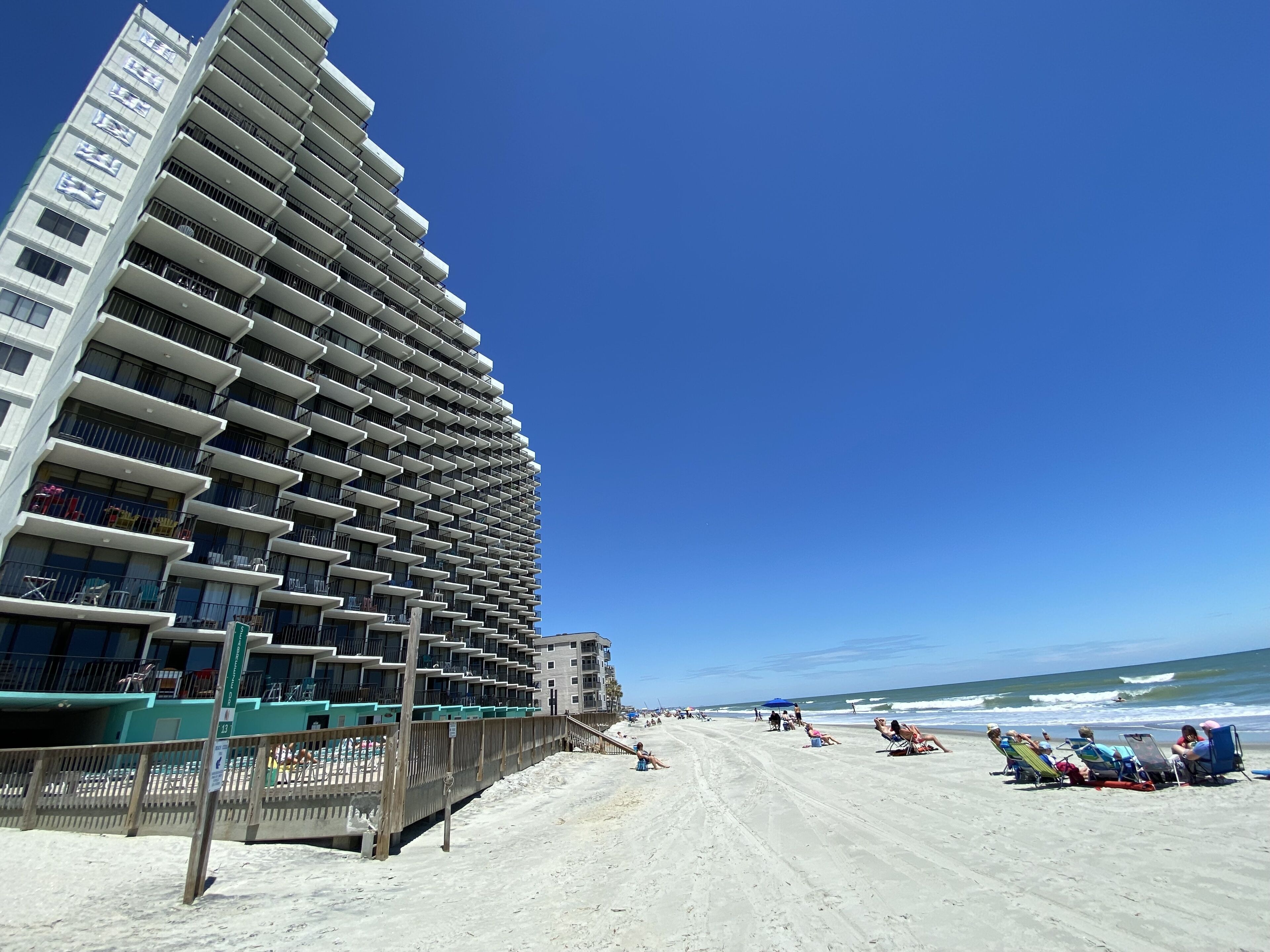 Ett hotell vid stranden med flera balkonger och en sandstrand i bakgrunden.