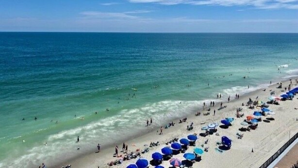 A beach with clear blue water, a sandy shore, and numerous umbrellas.