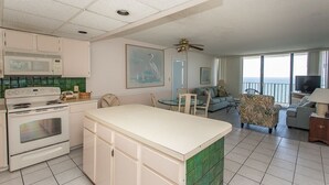 A kitchen with a white stove, a dining table, and chairs. There is a large window with a view of the ocean. - Royal Garden Resort 1605 2 Bedroom Condo by RedAwning (Murrells Inlet)