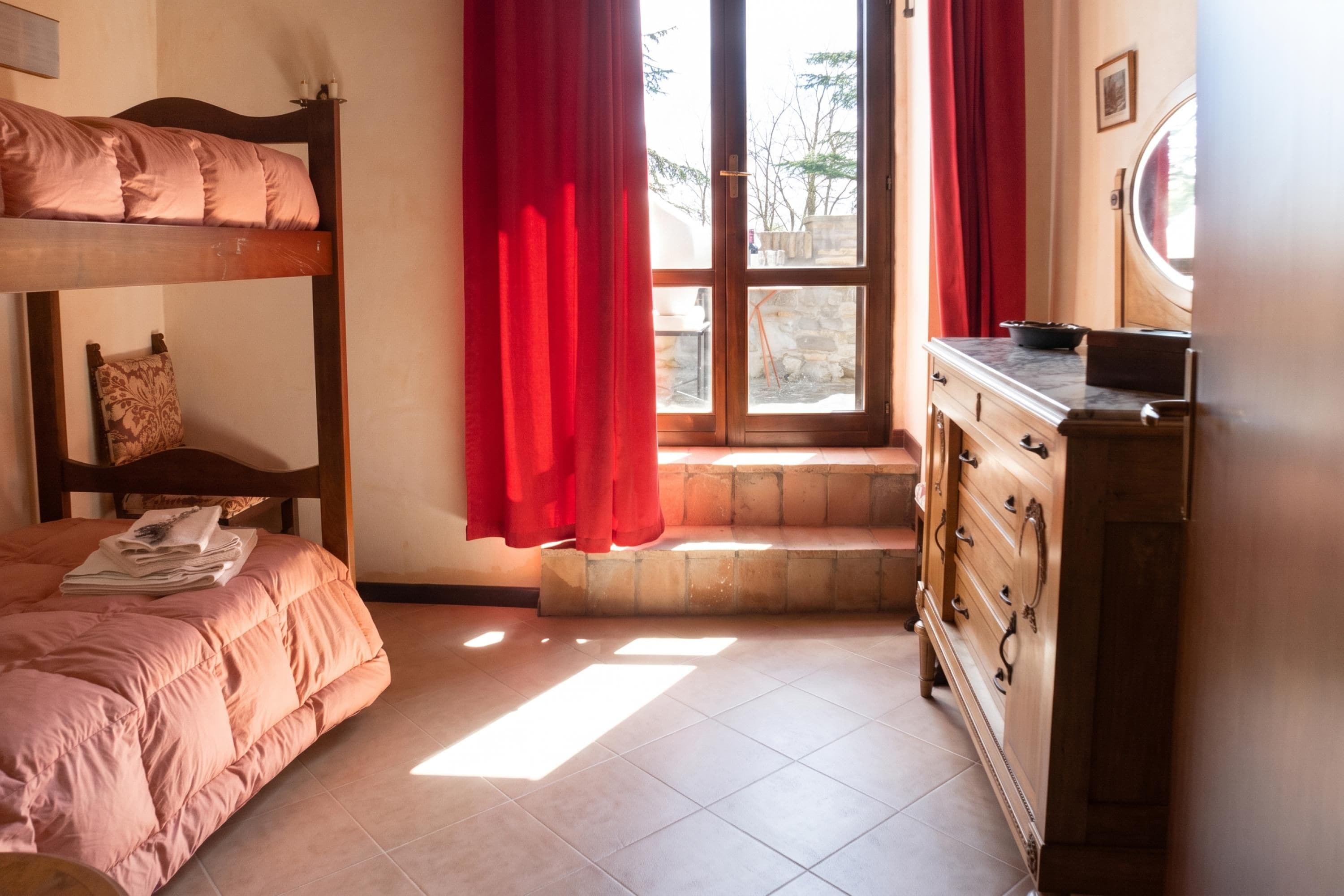 Ein Zimmer mit einem Etagenbett, einem Schminktisch und einem Fenster mit Vorhängen.