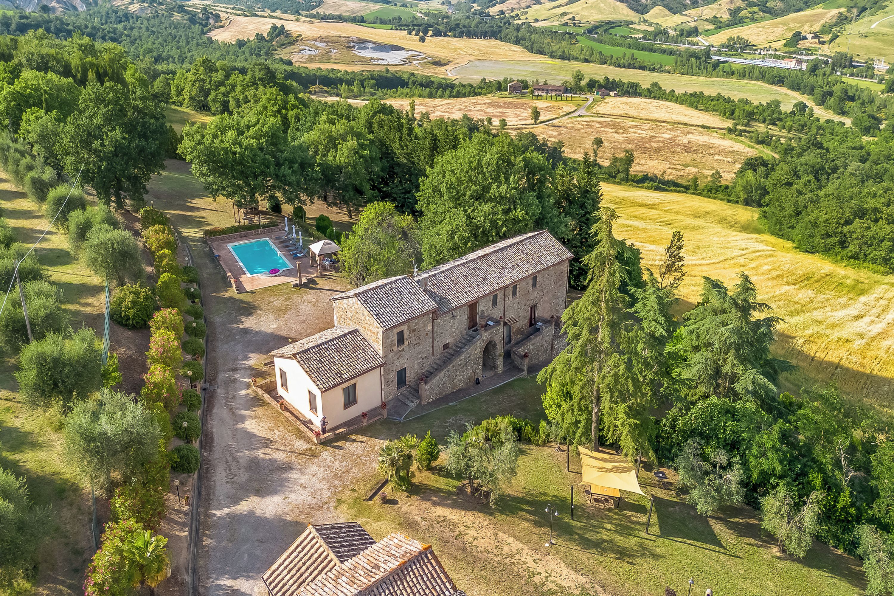 An aerial view of a property with a swimming pool, a stone building, and surrounding greenery.