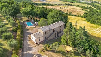 An aerial view of a property with a swimming pool, a stone building, and surrounding greenery.