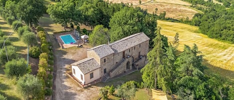 An aerial view of a property with a swimming pool, a stone building, and surrounding greenery.