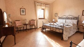 A bedroom with a bed, a desk, a chair, a small table, and a window with curtains.