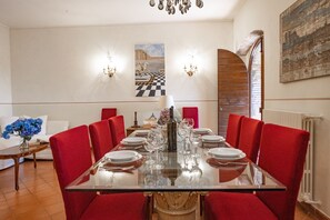 Uma sala de jantar com mesa de vidro posta para refeição, cadeiras estofadas vermelhas e um lustre.