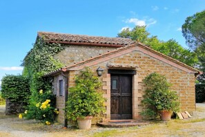 Un petit bâtiment en pierre avec un toit en tuiles, une porte en bois sombre et des plantes en pot.