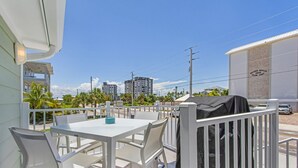 A balcony with a white table and chairs, a grill, and a view of palm trees and buildings. - Welcome To Coconut Dreams Fantastic Vacation Rental - 2633 Estero Blvd Unit A 3 Bedroom Home by RedAwning (Fort Myers Beach)
